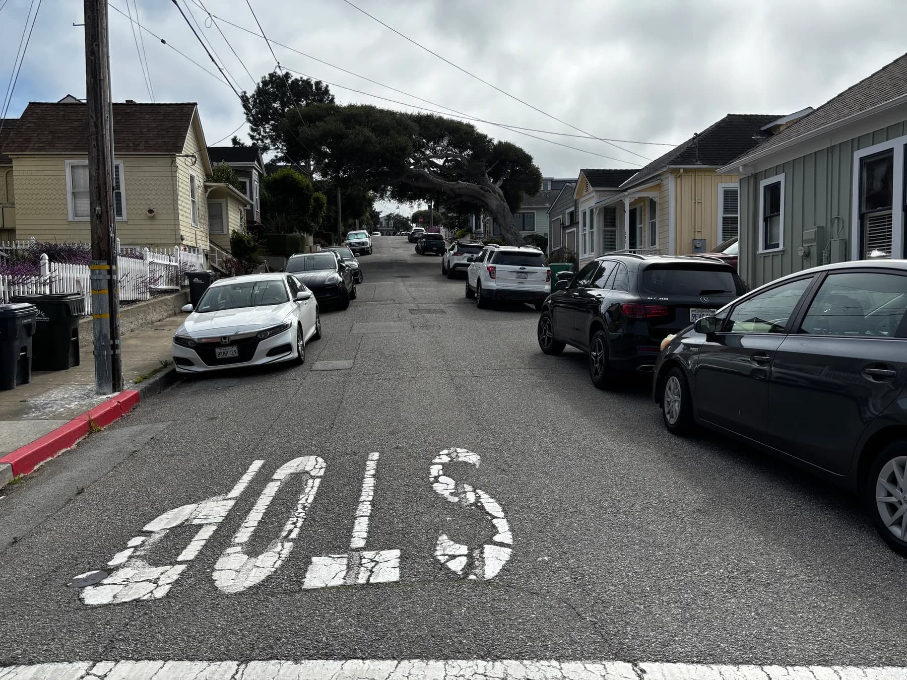 A narrow Pacific Grove street with cars parked on both sides, leaving room for one car to pass